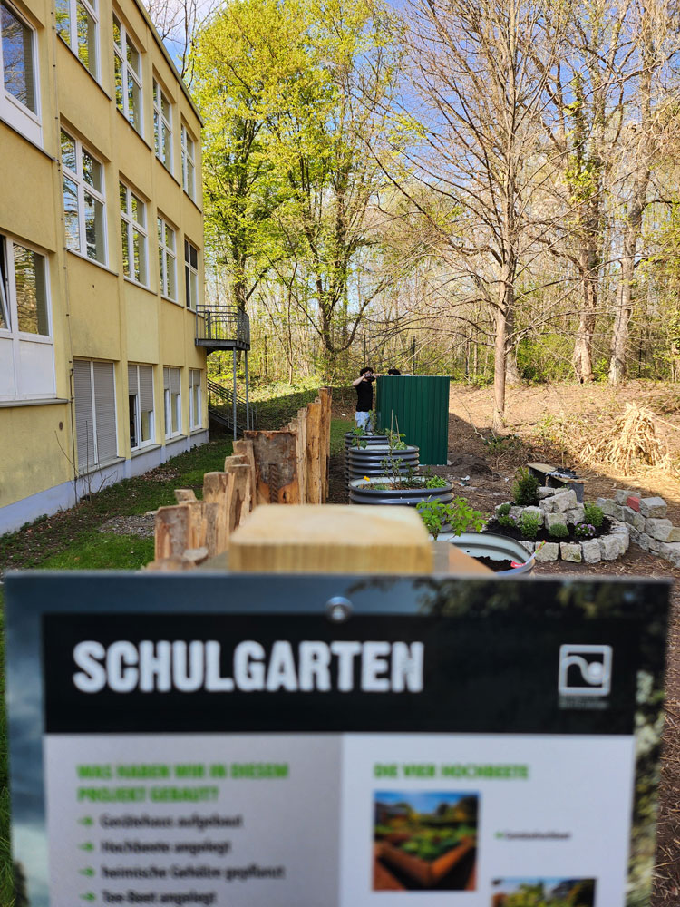 Vitavia Hochbeete und Gerätehaus im Schulgarten Dortmund neben dem Schulgebäude, davor ein Schild mit Aufschrift " Schulgarten"
