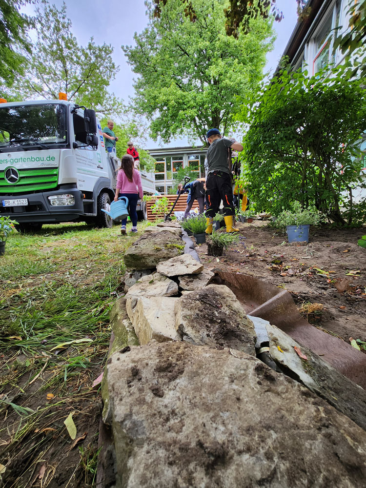 Aufbau Schulgarten: Kinder mit Gartenwerkzeug nebben einem LKW