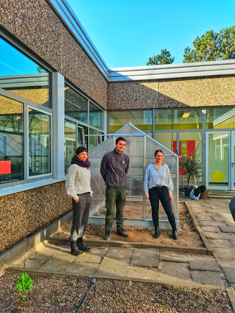 Schulgartenprojekt in Am Gymnasium in Neuss, Gruppenfoto der Kooperationspartner mit Gewächshaus im Hintergrund